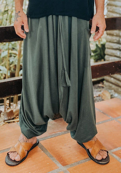 Calça Goa Nomads verde escuro em algodão penteado, com bolso lateral e cordão na cintura. Modelo em pé, vestindo sandálias.