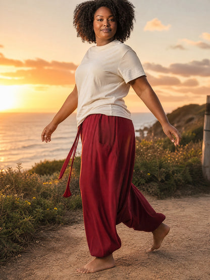 Calça Goa Vinho da Goa Nomads em algodão penteado, com bolso lateral e cordão na cintura. Modelo plus size em cenário de pôr do sol.