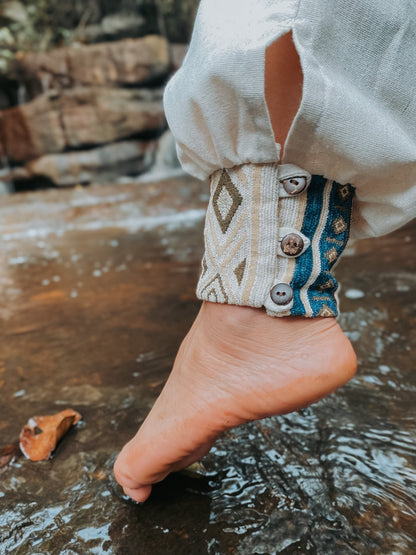 Goa Nomads cream linen pants with embroidered ankle cuff featuring geometric patterns and blue accents, fastened with buttons.